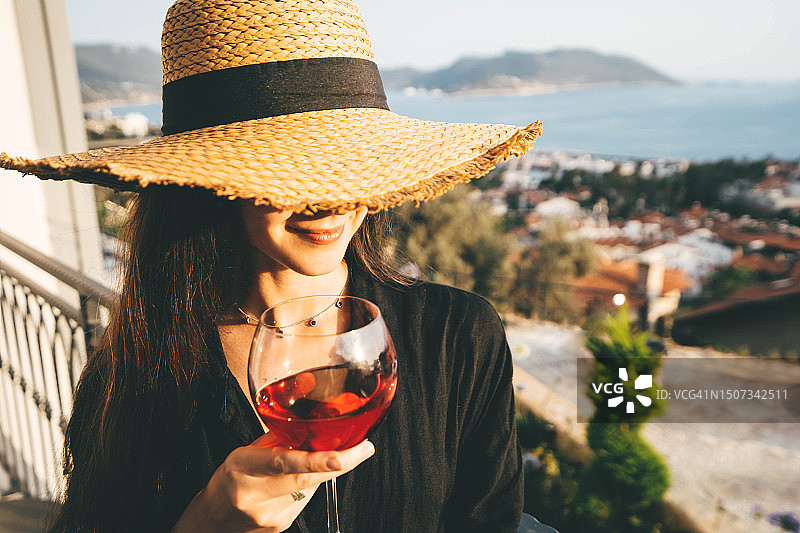 戴着柳条帽，在私人别墅阳台上喝玫瑰酒的女人图片素材