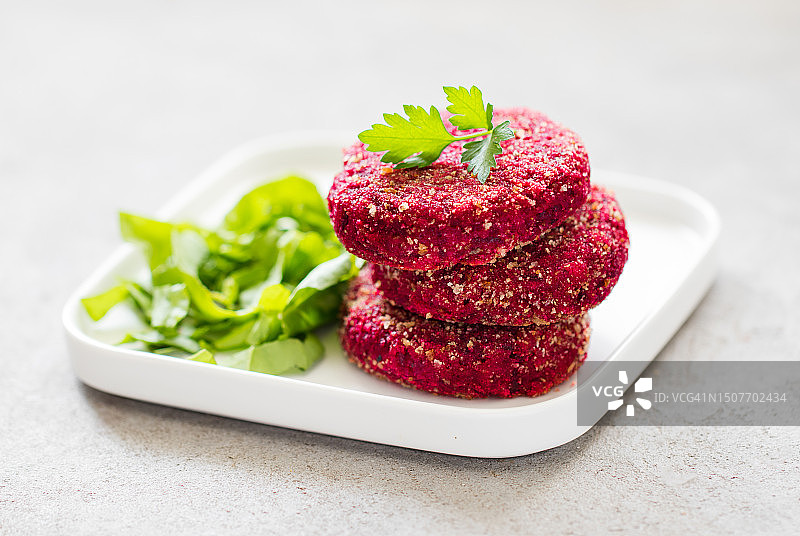 盘中搭配绿色沙拉的甜菜根炸肉饼，浅灰色背景图片素材