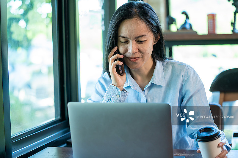 亚洲女人在咖啡店使用智能手机和笔记本电脑工作图片素材
