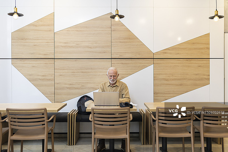 微笑的老年男人在餐厅使用笔记本电脑工作图片素材
