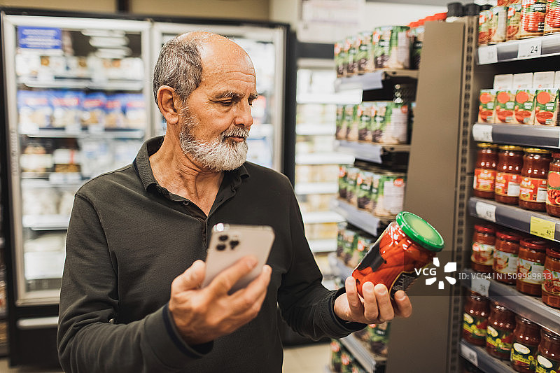 老年男人在超市购物，并使用手机阅读产品评论图片素材
