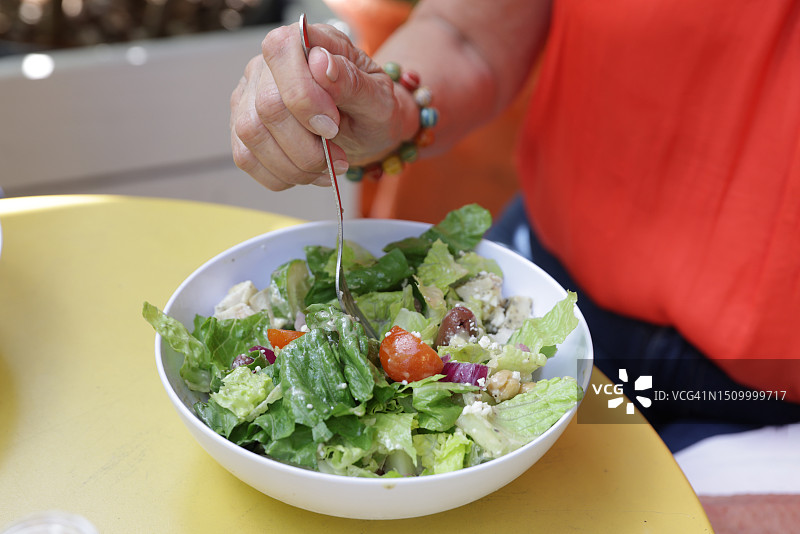 中年拉丁裔女人在户外餐桌上吃沙拉的细节图片素材