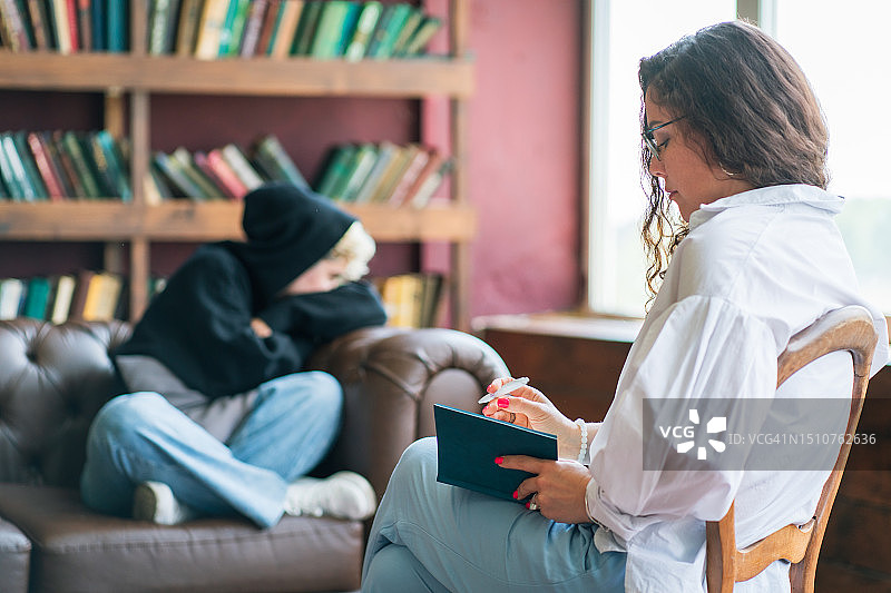 药物治疗与青少年戒瘾，治疗过程。女治疗师做笔记并帮助沙发上的少女图片素材