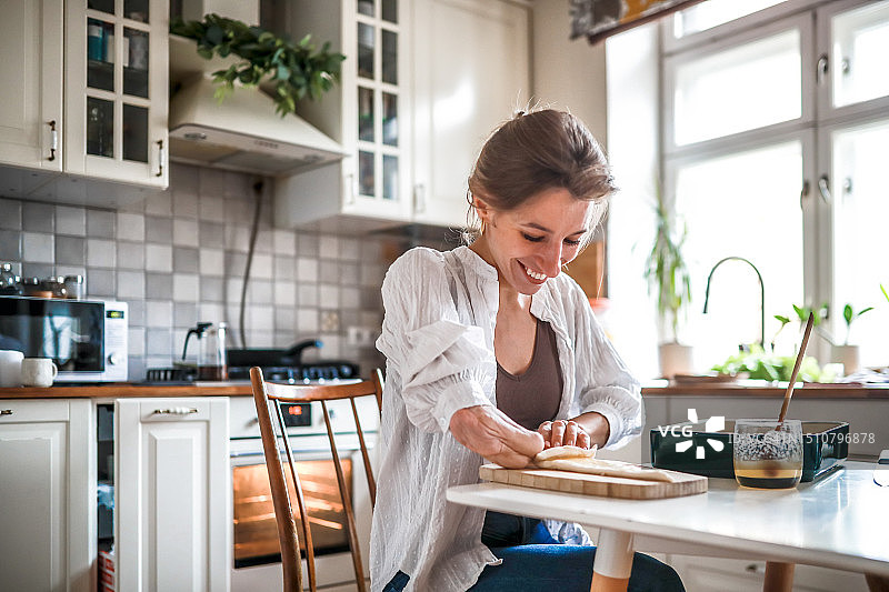 温馨厨房的魔法：面带微笑的漂亮女人用截肢的手臂在绿色陶瓷烤模中烘烤蜂蜜牛角面包。图片素材