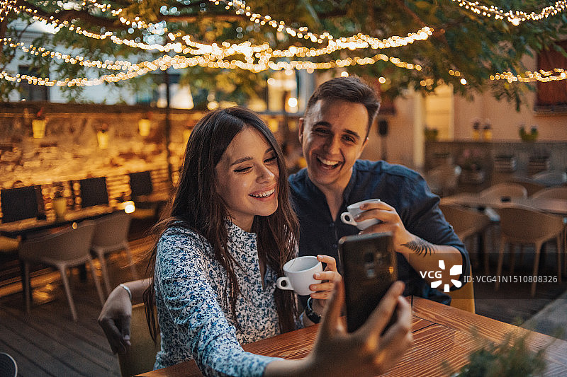情侣在咖啡馆享受夜晚，美丽的灯笼营造出浪漫的氛围，他们看起来都很快乐和放松图片素材