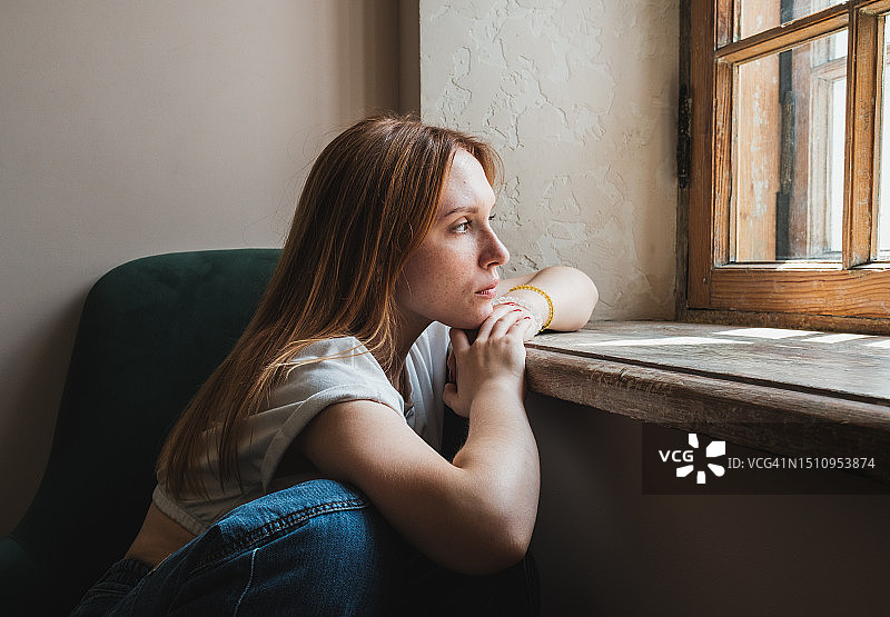 悲伤的少女望着窗外，沮丧的青少年在家中图片素材