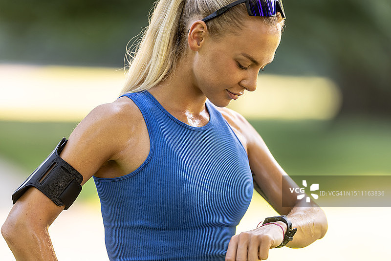 在公园查看智能手表运动表现的金发女运动员画像图片素材