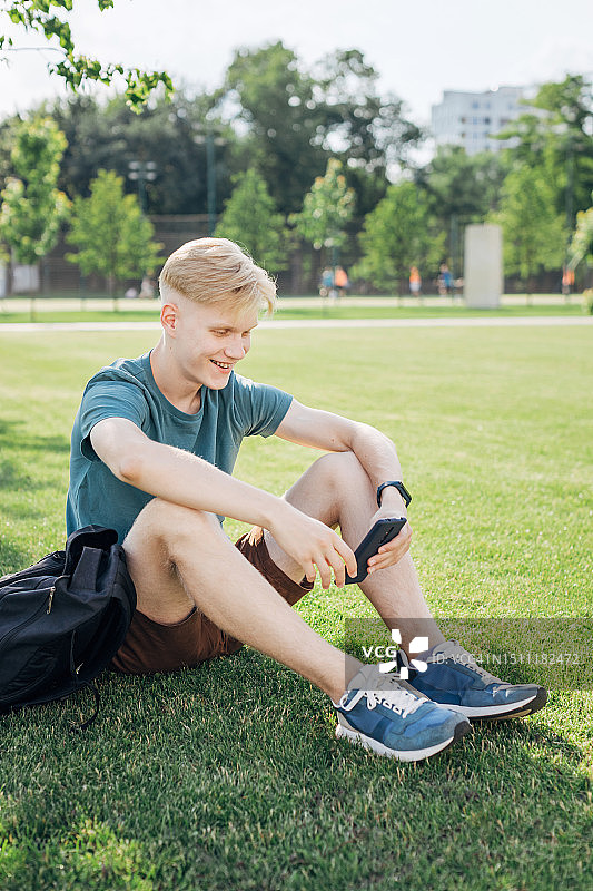 年轻男人坐在草地上使用智能手机图片素材