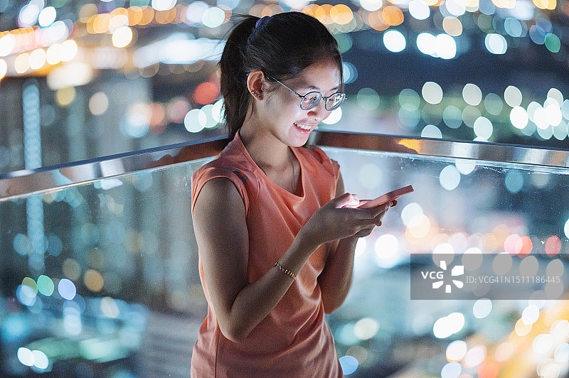 Z世代亚洲青少年在屋顶夜晚使用AI聊天机器人打字，充满乐趣和快乐图片素材