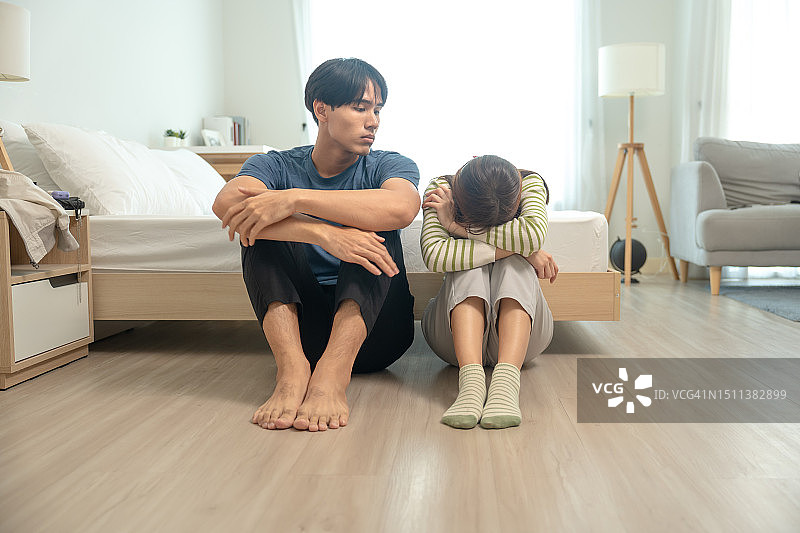 令人心碎的瞬间 - 两个年轻男人坐在床边，紧紧地拥抱在一起。他们双膝靠近，脸上充满了悲伤、忧愁和愤怒，在激烈的争吵之后图片素材