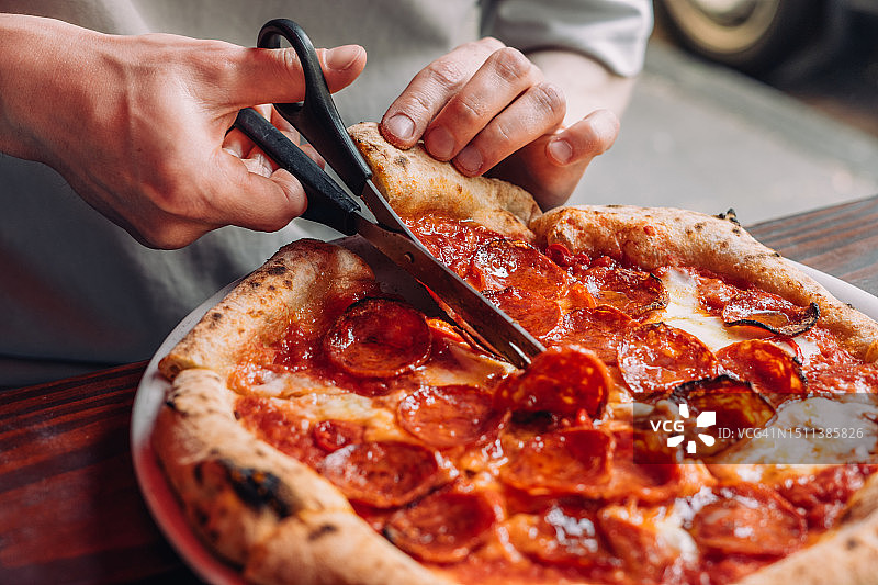 年轻男人用剪刀切割新鲜出炉的披萨图片素材