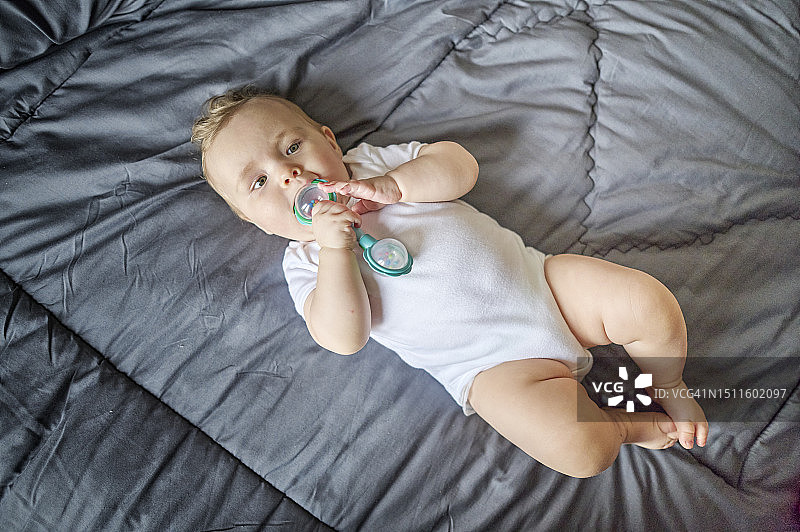 嘴里含着玩具的可爱女宝宝躺在公寓的床上图片素材