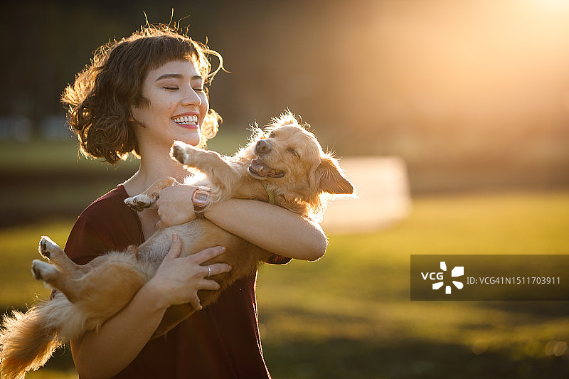 在公园里抱着她的狗的快乐女人图片素材