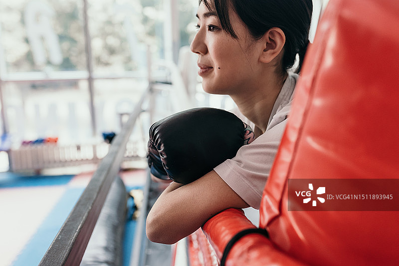 年轻的亚洲女拳击手站在拳击台一角。图片素材