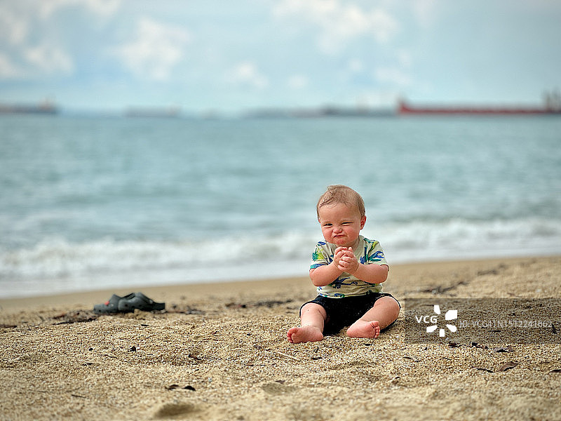 年轻的男婴坐在沙滩上玩耍图片素材