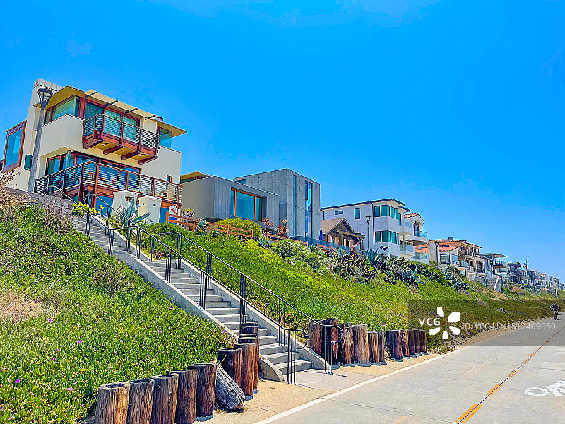 曼哈顿海滩自行车道上的人们上方的山坡上的房屋图片素材