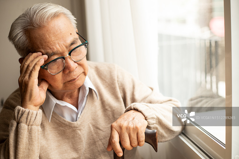 年长的亚洲男人坐在桌旁，头痛难忍图片素材