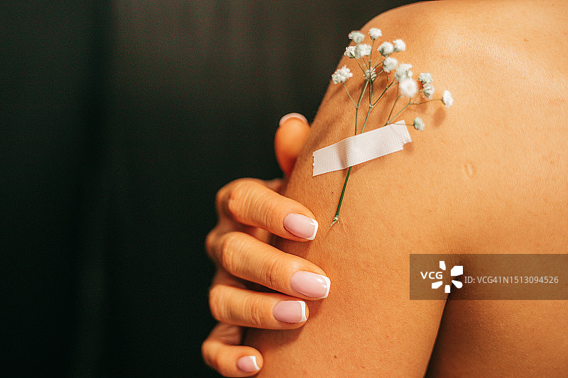 黑色背景上，一位无法辨认的女性的肩膀，带有精致的小花和胶带，护肤、美黑、美容行业、自我护理、自爱概念图片素材