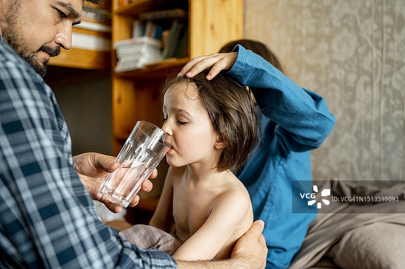 父亲在家给生病的儿子喂水图片素材