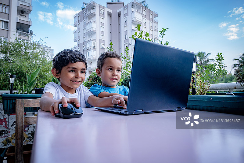 两个男孩在阳台上使用笔记本电脑。图片素材