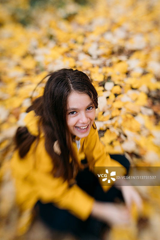 穿黄色雨衣的女孩坐在满是秋叶的公园里图片素材