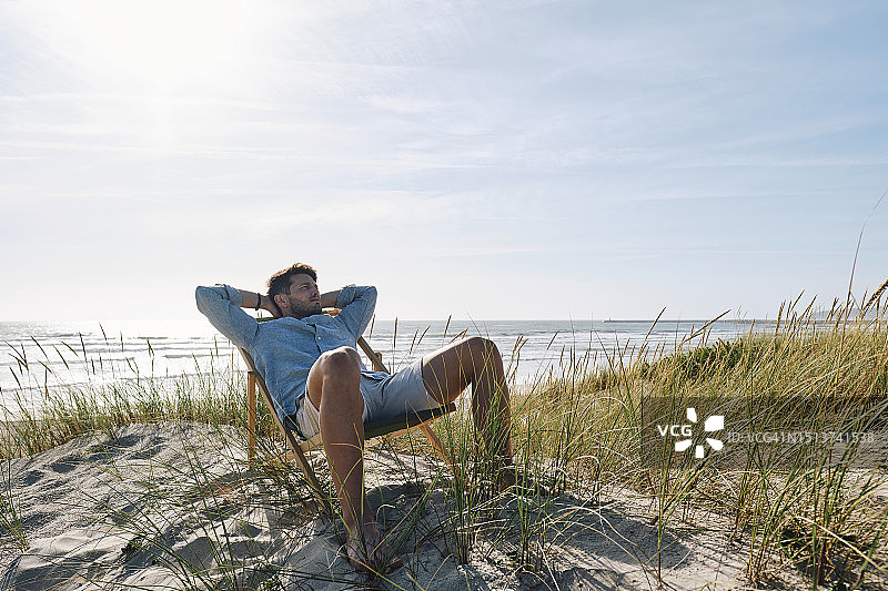 男人在阳光明媚的沙滩上坐在椅子上放松图片素材