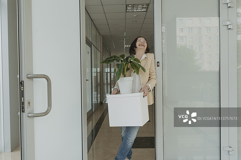 快乐的老年女商人抱着盆栽站在办公室门口图片素材