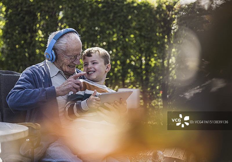 快乐的老年男人戴着无线耳机与孙子玩耍图片素材