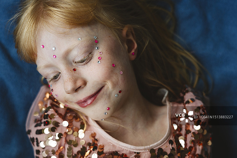 脸上贴着水晶的金发女孩躺在蓝色织物上图片素材