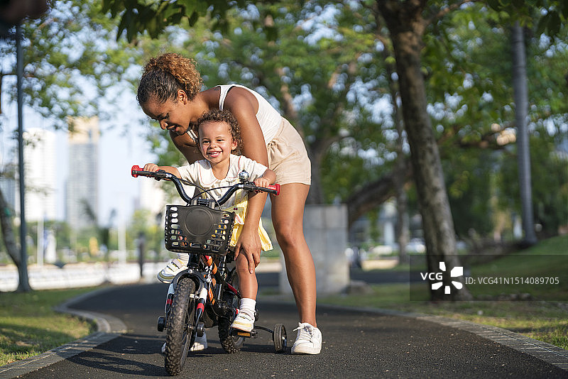 年轻母亲在公园里教女儿骑自行车图片素材