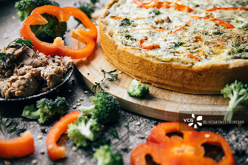 新鲜美味馅饼，酵母面团，红椒、金枪鱼和西兰花馅料，撒上奶酪，放在厨房桌子上，周围是主要食材。图片素材