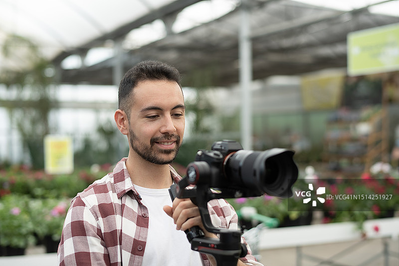 视频操作员使用云台和微单在温室现场录制视频，穿着格子衬衫微笑图片素材