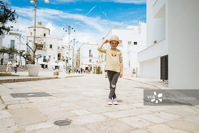 六岁女孩参观古镇，看着镜头，拿着帽子图片素材