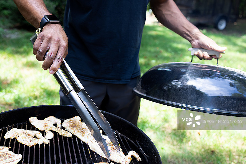黑人男子在户外烧烤架上烤鸡肉片图片素材