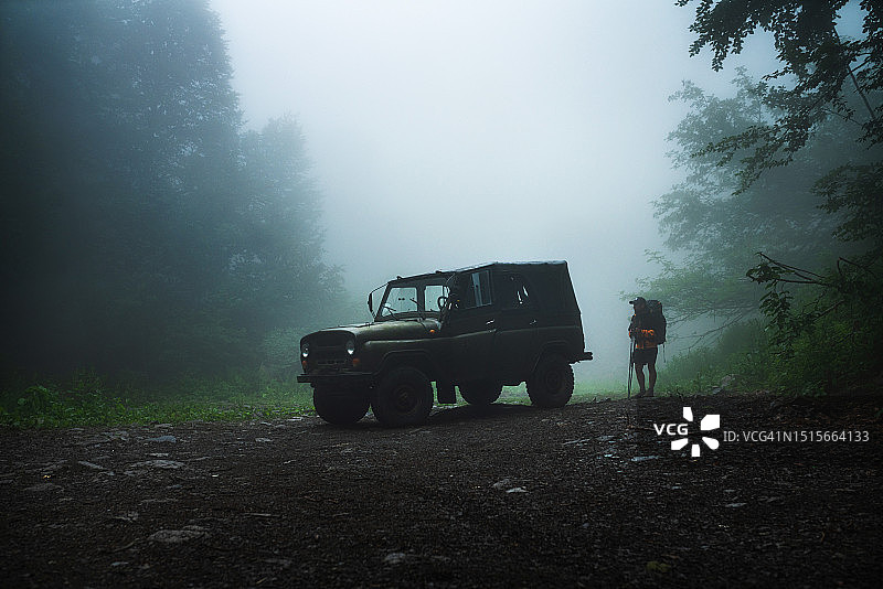 徒步者站在雾气弥漫的森林道路上的旧越野车旁图片素材