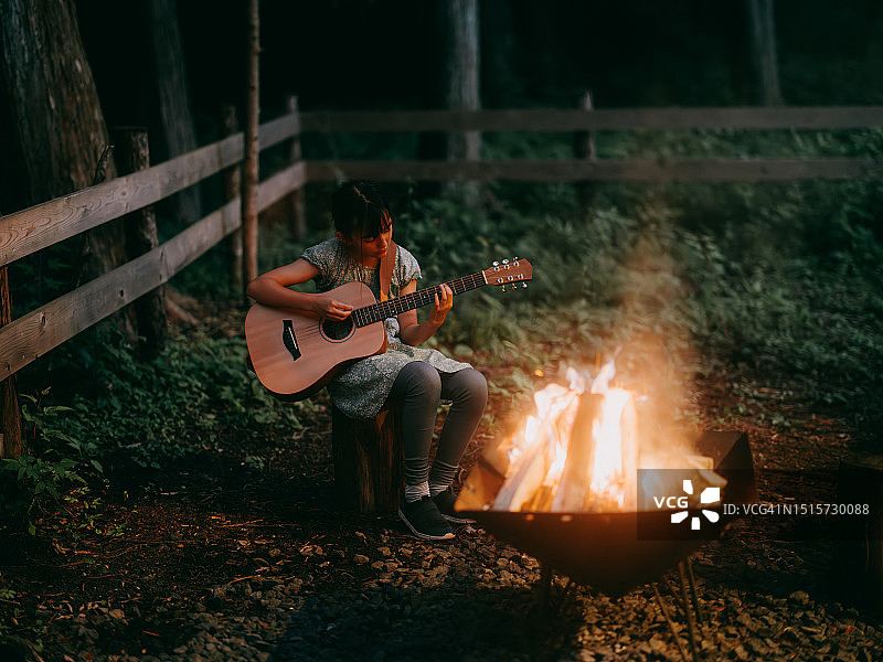 年轻女孩在夜晚篝火旁弹吉他图片素材