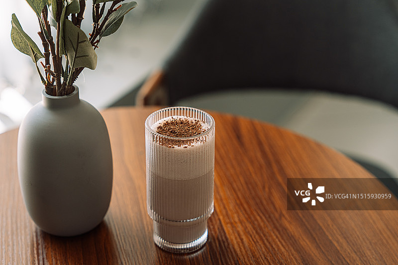 木桌花瓶旁玻璃杯中的巧克力奶昔图片素材