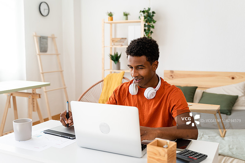 黑人男子在使用笔记本电脑时做笔记图片素材