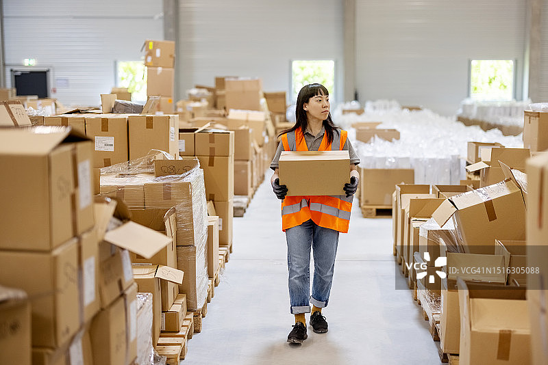 亚洲女人在物流中心的仓库里搬运包裹图片素材
