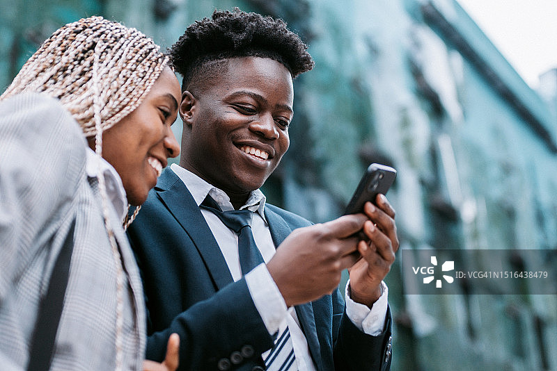 在户外用手机看照片的乐趣。两个年轻黑人在市中心使用智能手机图片素材