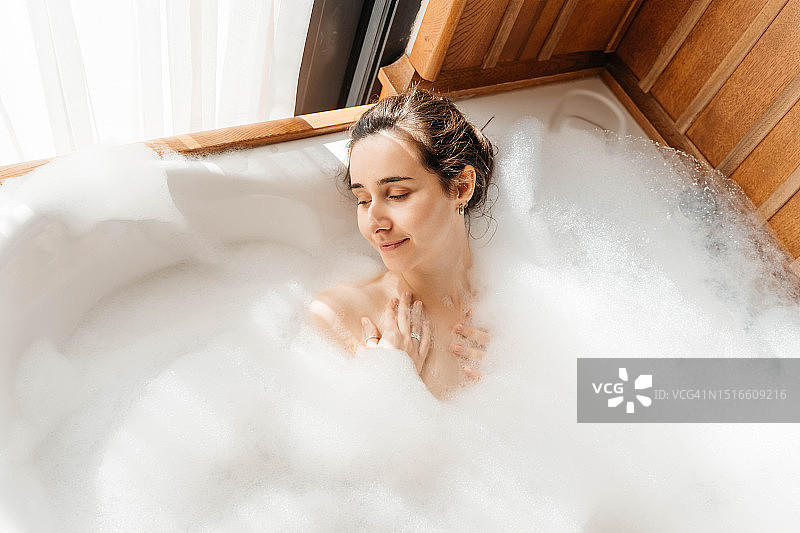 年轻女人在满是泡沫的浴缸里放松，关爱自己，呵护心理健康图片素材