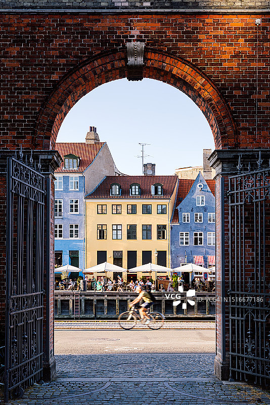 阳光明媚的夏日，骑自行车的人经过丹麦哥本哈根新港图片素材