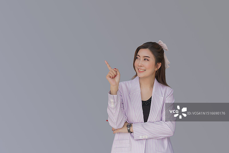 身穿紫色西装，用手势提供空白和广告及公告信息的自信女商人，灰色背景图片素材