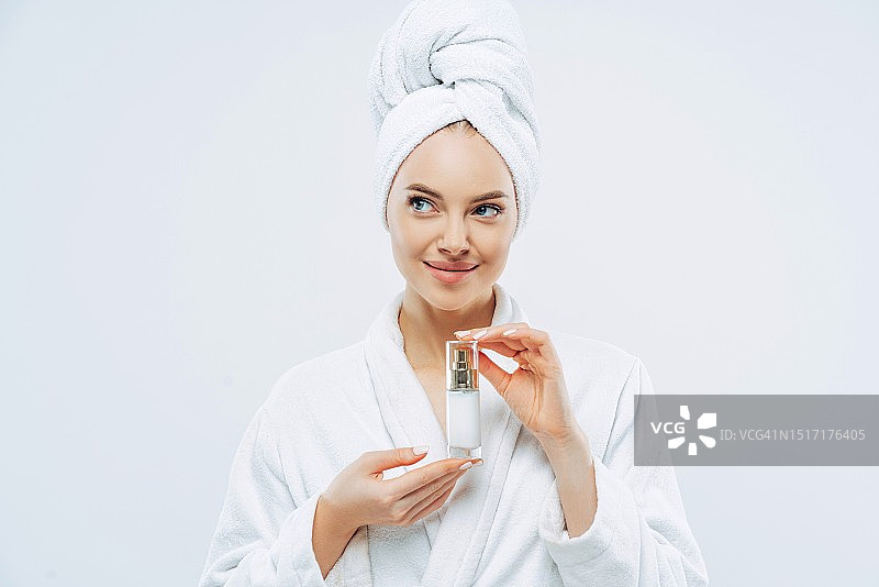 年轻女子在白色背景前涂抹保湿霜的肖像图片素材