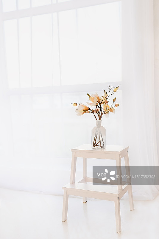 玻璃花瓶中粉色人造玉兰花束，置于白色梯凳上图片素材
