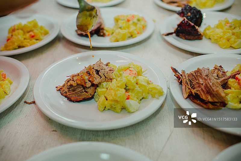 用勺子调味肉类菜肴，土豆沙拉摆放在桌子上，还有许多其他菜肴的特写图片素材