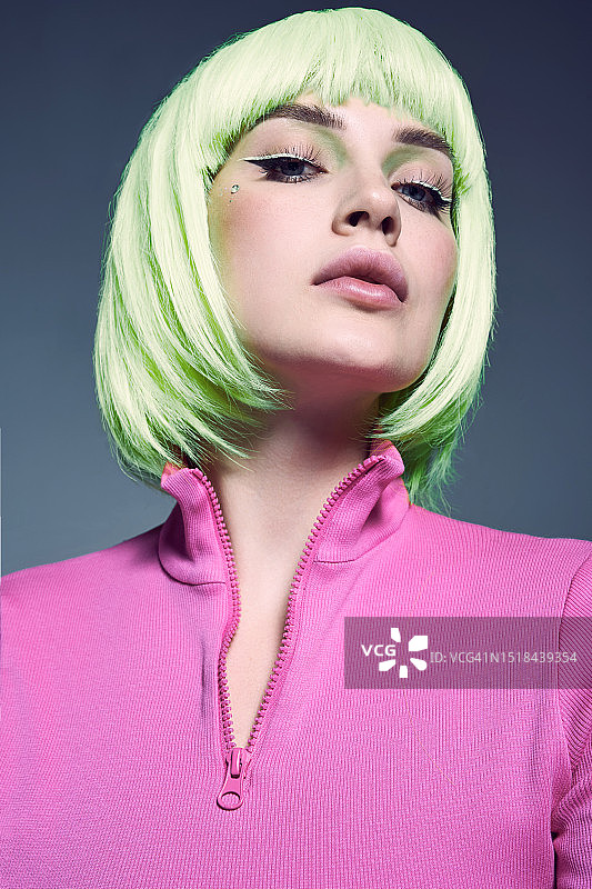 佩戴绿色假发、身穿粉色高领衫的时尚美女，灰色背景图片素材