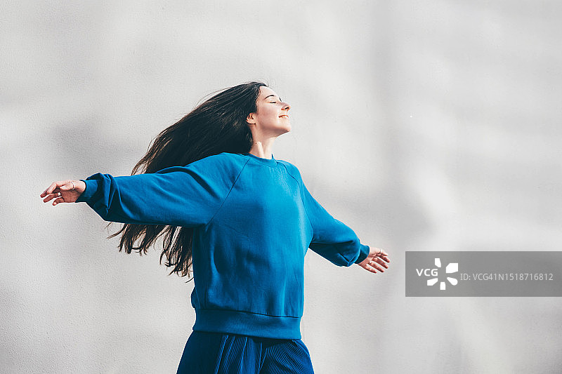 身穿蓝色运动衫的年轻女人靠墙站立图片素材