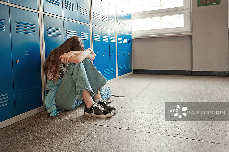 焦虑的少女坐在学校的地板上图片素材