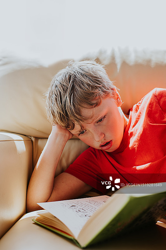 小男孩侧卧在沙发上读书图片素材